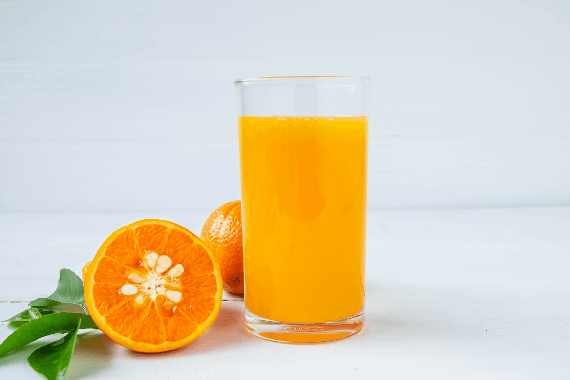Orange juice in a glass next to oranges